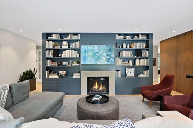 living room featuring built in shelves, wood walls, and a high end fireplace