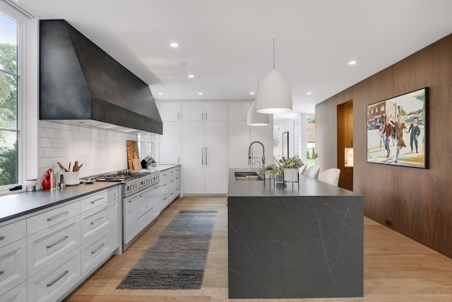 kitchen featuring a wealth of natural light, white cabinetry, wall chimney range hood, and a large island with sink