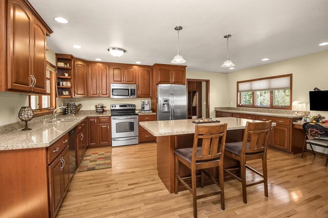 kitchen with light wood-type flooring, light stone counters, a kitchen island, stainless steel appliances, and pendant lighting