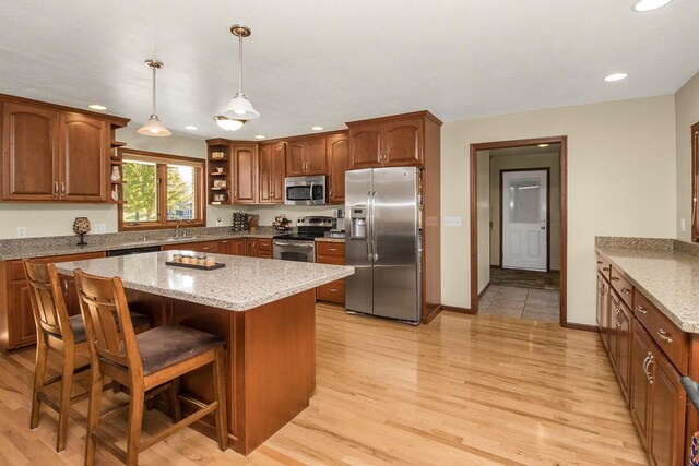 kitchen featuring a kitchen island, light stone counters, stainless steel appliances, light hardwood / wood-style flooring, and decorative light fixtures