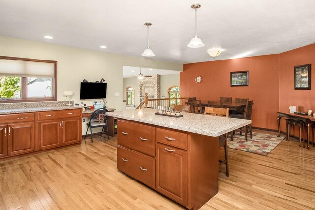 kitchen with a kitchen island, ceiling fan, light hardwood / wood-style floors, a breakfast bar area, and decorative light fixtures