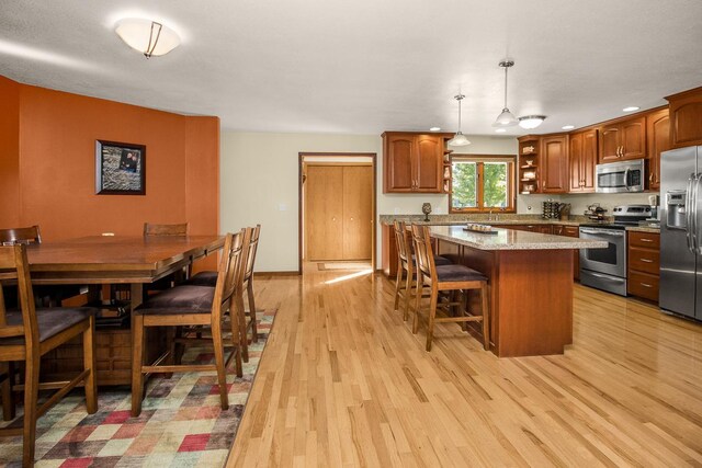 kitchen featuring pendant lighting, light hardwood / wood-style flooring, a breakfast bar, stainless steel appliances, and light stone countertops