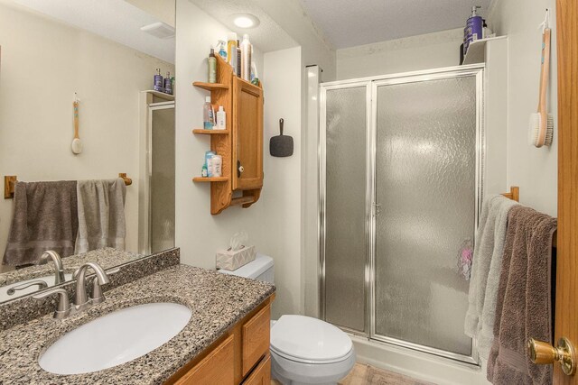 bathroom with a textured ceiling, walk in shower, vanity, and toilet