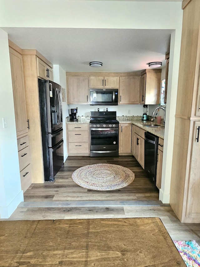 kitchen with light brown cabinets, dark wood-type flooring, sink, and black appliances