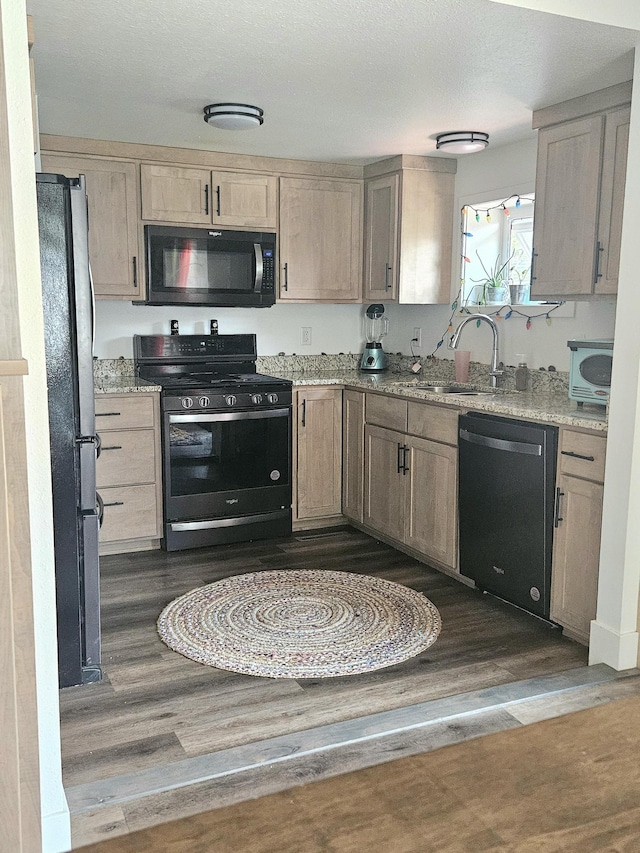 kitchen with light stone counters, light brown cabinets, dark hardwood / wood-style flooring, black appliances, and sink