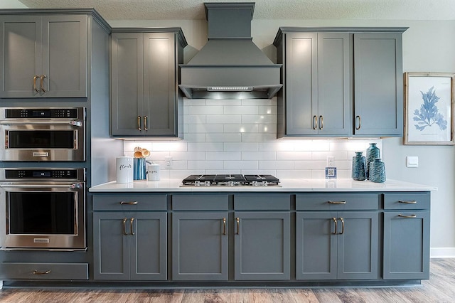 kitchen with hardwood / wood-style flooring, custom range hood, gray cabinetry, stainless steel appliances, and backsplash