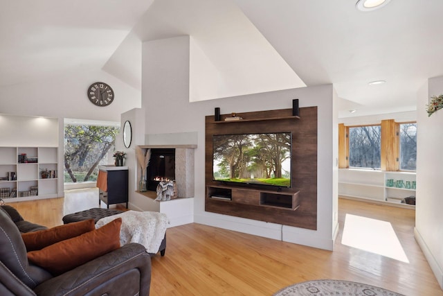 living room featuring built in features, light hardwood / wood-style floors, and vaulted ceiling