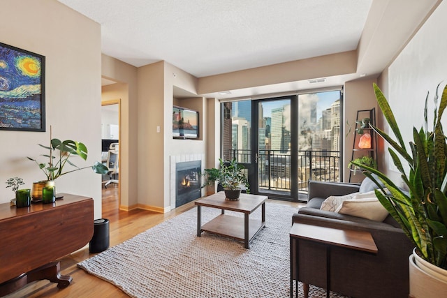 living room with a tiled fireplace, a textured ceiling, light wood-type flooring, and baseboards