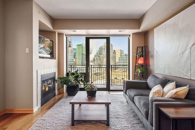 living area with a view of city, visible vents, light wood-style floors, a tile fireplace, and baseboards