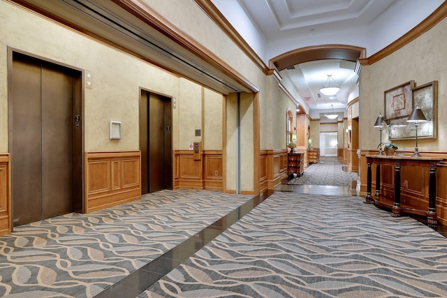 corridor with a wainscoted wall, a tray ceiling, arched walkways, and elevator