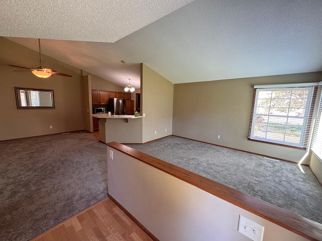 carpeted spare room featuring a textured ceiling, ceiling fan with notable chandelier, and vaulted ceiling