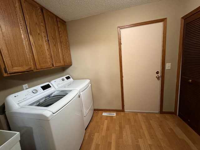 laundry area with a textured ceiling, washing machine and dryer, light hardwood / wood-style floors, and cabinets