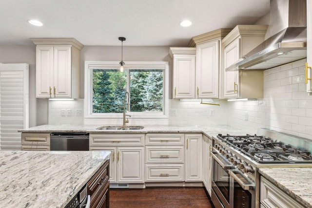 kitchen with tasteful backsplash, wall chimney exhaust hood, stainless steel appliances, sink, and hanging light fixtures