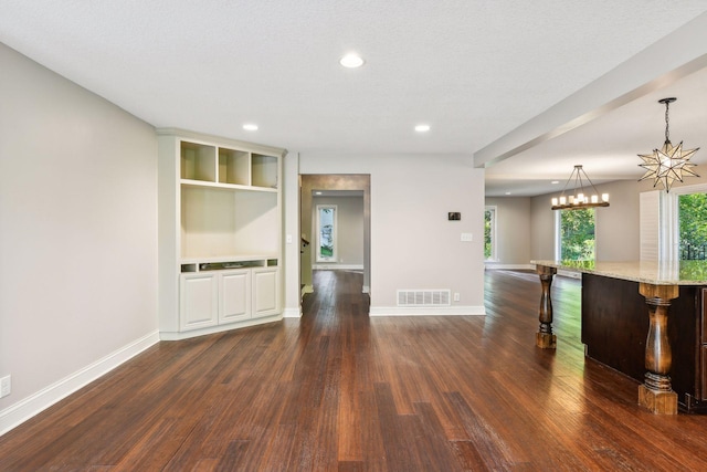 empty room with dark wood-type flooring, a textured ceiling, and a notable chandelier