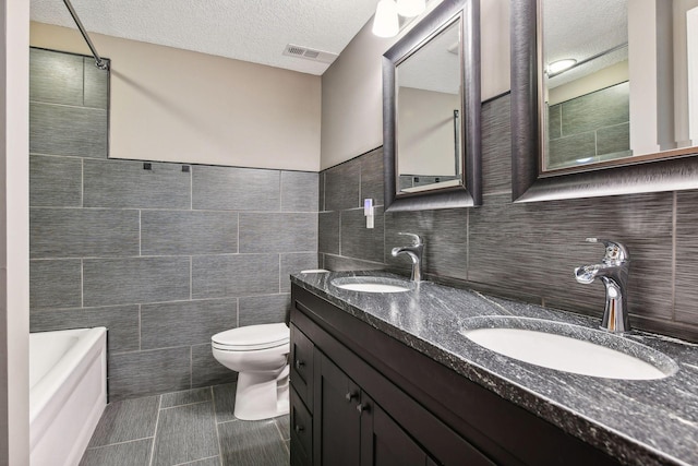 bathroom with a textured ceiling, vanity, tile walls, and toilet