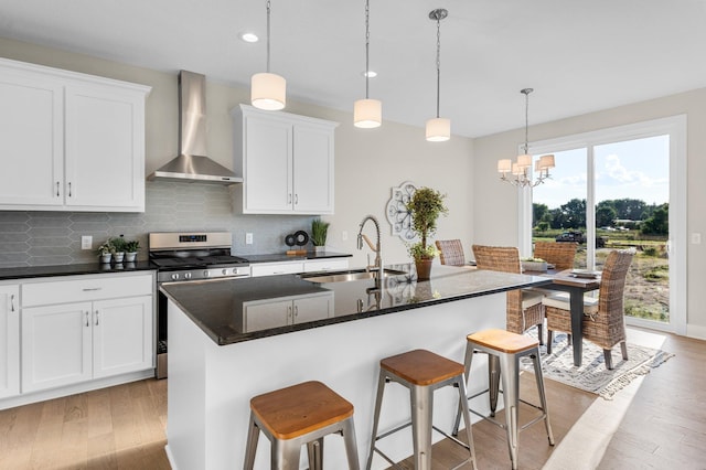 kitchen with light hardwood / wood-style floors, a kitchen island with sink, sink, wall chimney range hood, and stainless steel range