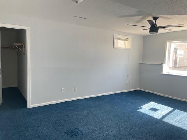 unfurnished bedroom featuring ceiling fan, a walk in closet, a textured ceiling, and dark carpet