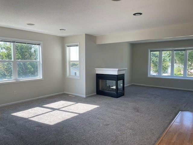 unfurnished living room with a multi sided fireplace and dark carpet