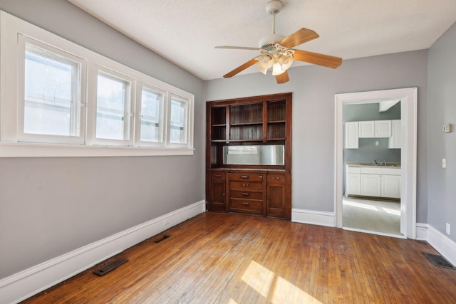 empty room featuring hardwood / wood-style flooring, a sink, visible vents, and baseboards