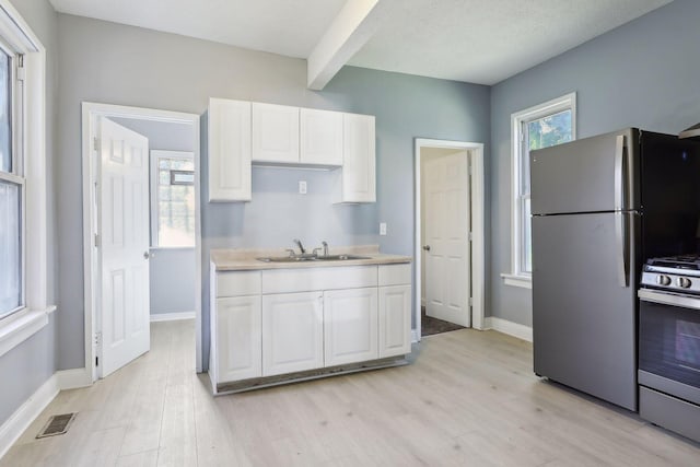 kitchen with a sink, visible vents, white cabinets, freestanding refrigerator, and gas range