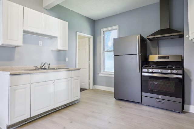 kitchen featuring white cabinets, appliances with stainless steel finishes, wall chimney range hood, and sink