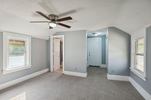 unfurnished bedroom featuring lofted ceiling, a textured ceiling, carpet flooring, and baseboards