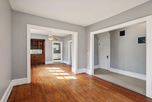 unfurnished room with a ceiling fan, visible vents, baseboards, and hardwood / wood-style flooring