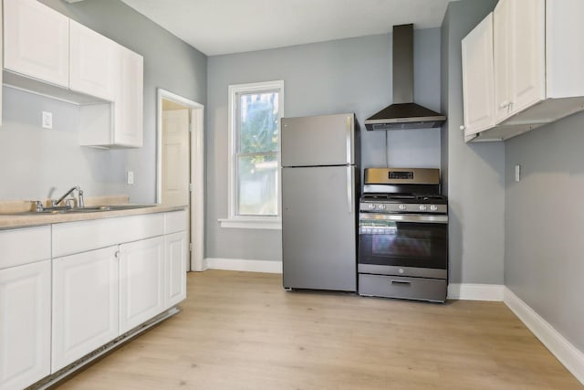 kitchen with stainless steel appliances, wall chimney range hood, a sink, and white cabinets