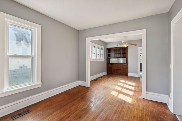 spare room featuring hardwood / wood-style flooring, baseboards, visible vents, and ceiling fan