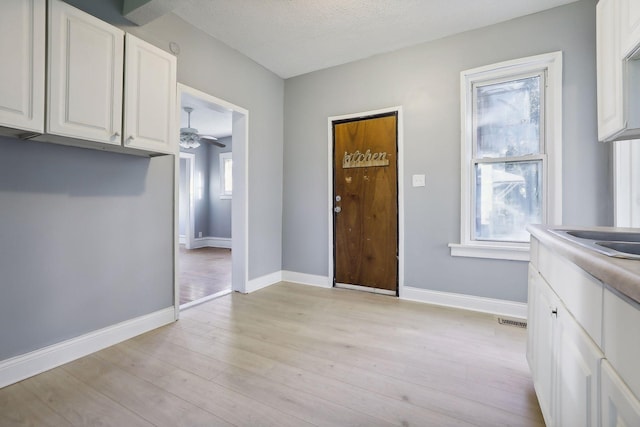 kitchen with visible vents, light wood-style floors, white cabinets, a textured ceiling, and baseboards