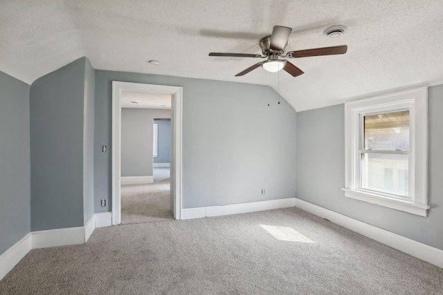 empty room featuring a textured ceiling, visible vents, baseboards, vaulted ceiling, and carpet