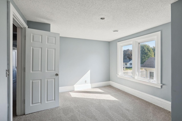 empty room with carpet floors, baseboards, and a textured ceiling