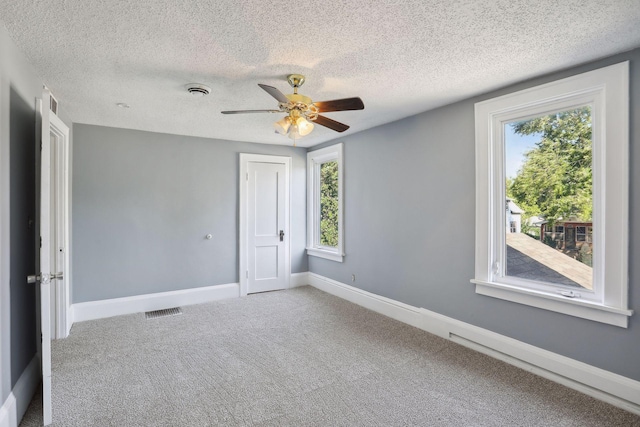 carpeted spare room with ceiling fan, a textured ceiling, visible vents, and baseboards