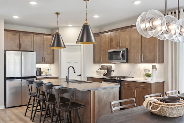 kitchen featuring pendant lighting, sink, backsplash, appliances with stainless steel finishes, and light hardwood / wood-style floors