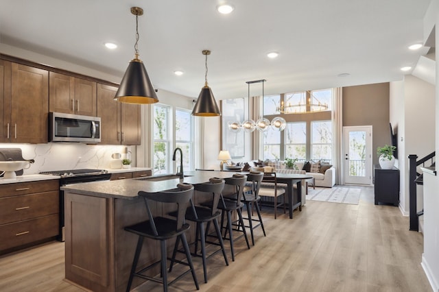 kitchen with dark brown cabinetry, sink, a center island with sink, electric stove, and light wood-type flooring