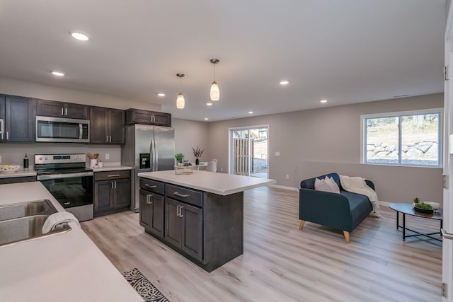 kitchen with dark brown cabinets, appliances with stainless steel finishes, light hardwood / wood-style flooring, pendant lighting, and a center island