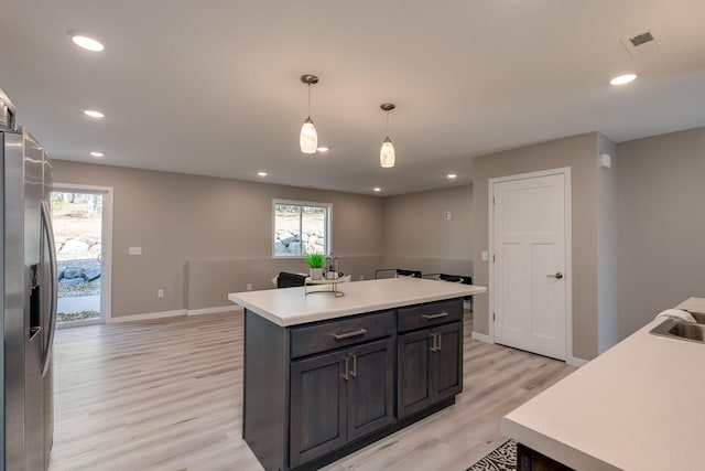 kitchen with a kitchen island, hanging light fixtures, stainless steel refrigerator with ice dispenser, sink, and light wood-type flooring