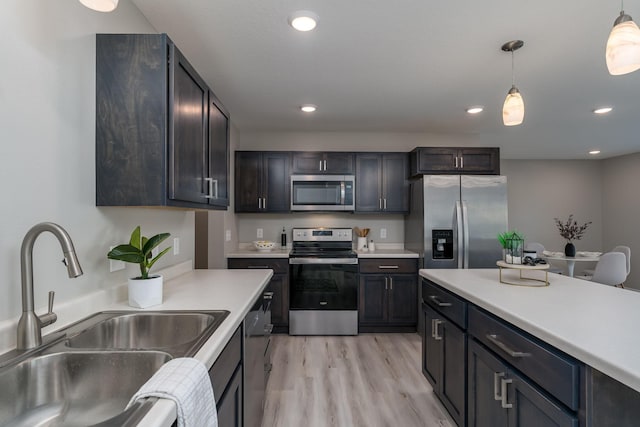 kitchen featuring appliances with stainless steel finishes, sink, light wood-type flooring, dark brown cabinetry, and pendant lighting