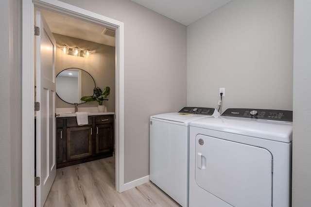 clothes washing area with washing machine and dryer and light wood-type flooring