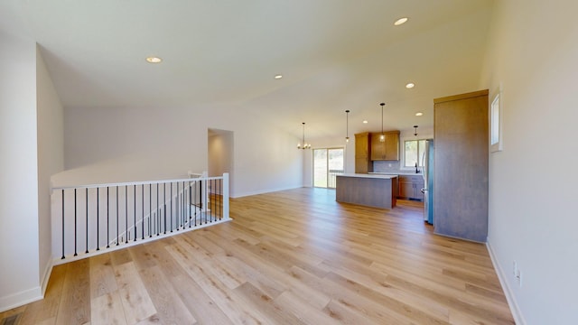 unfurnished living room featuring light hardwood / wood-style floors, vaulted ceiling, and a notable chandelier