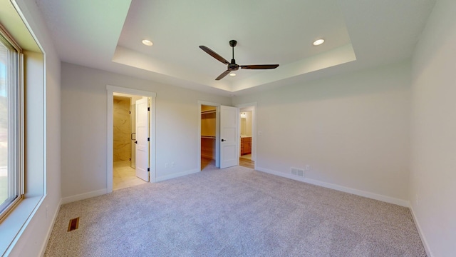 unfurnished bedroom featuring ceiling fan, ensuite bath, a raised ceiling, and light carpet