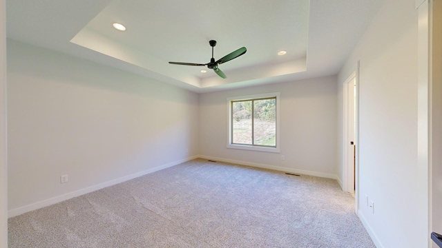 carpeted spare room with a tray ceiling and ceiling fan