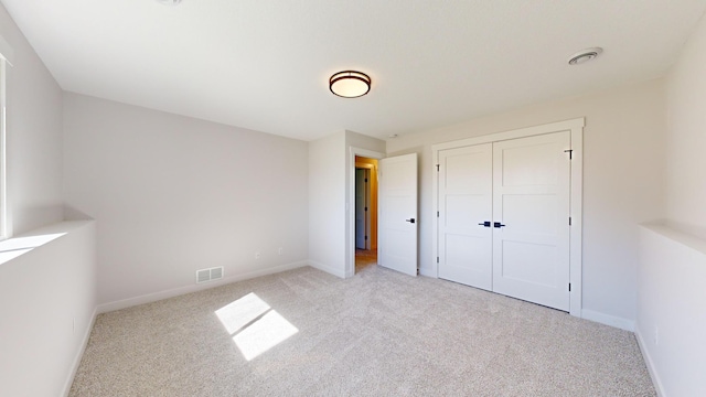 unfurnished bedroom with light colored carpet and a closet