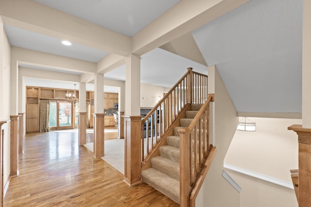 stairs with hardwood / wood-style floors, lofted ceiling with beams, and an inviting chandelier