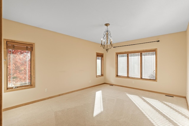 carpeted empty room featuring a healthy amount of sunlight and an inviting chandelier