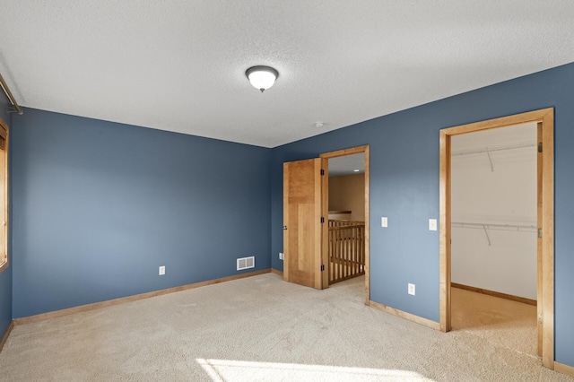 unfurnished bedroom featuring a textured ceiling, a walk in closet, light colored carpet, and a closet