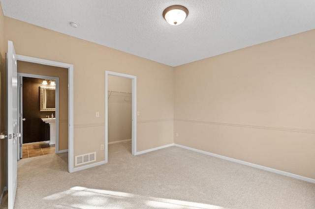 unfurnished bedroom featuring a closet, a textured ceiling, light colored carpet, and a walk in closet