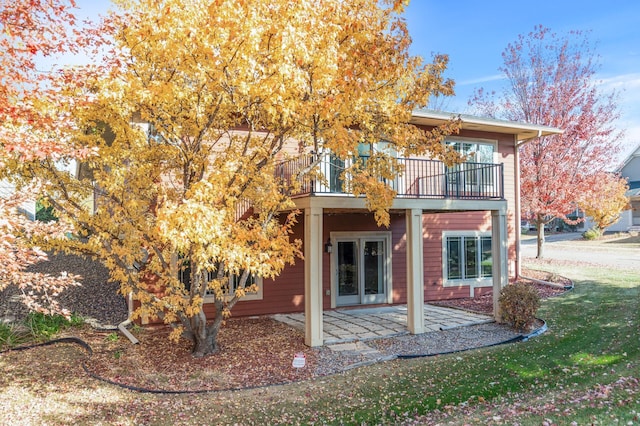 back of property with a balcony, a patio area, and a lawn