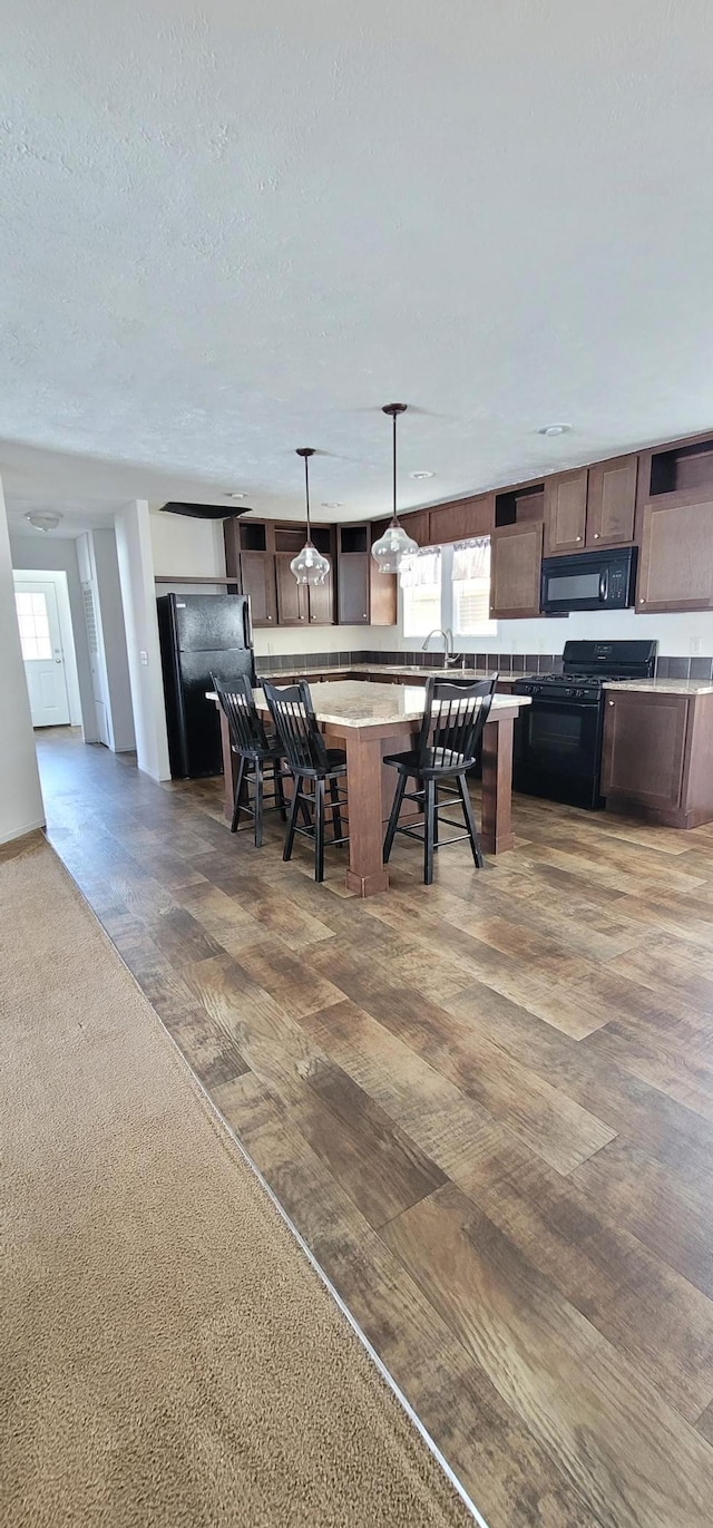 kitchen featuring dark brown cabinetry, hanging light fixtures, light countertops, a textured ceiling, and black appliances