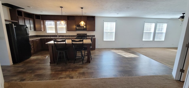 kitchen featuring dark brown cabinetry, a kitchen island, open floor plan, a kitchen breakfast bar, and black appliances